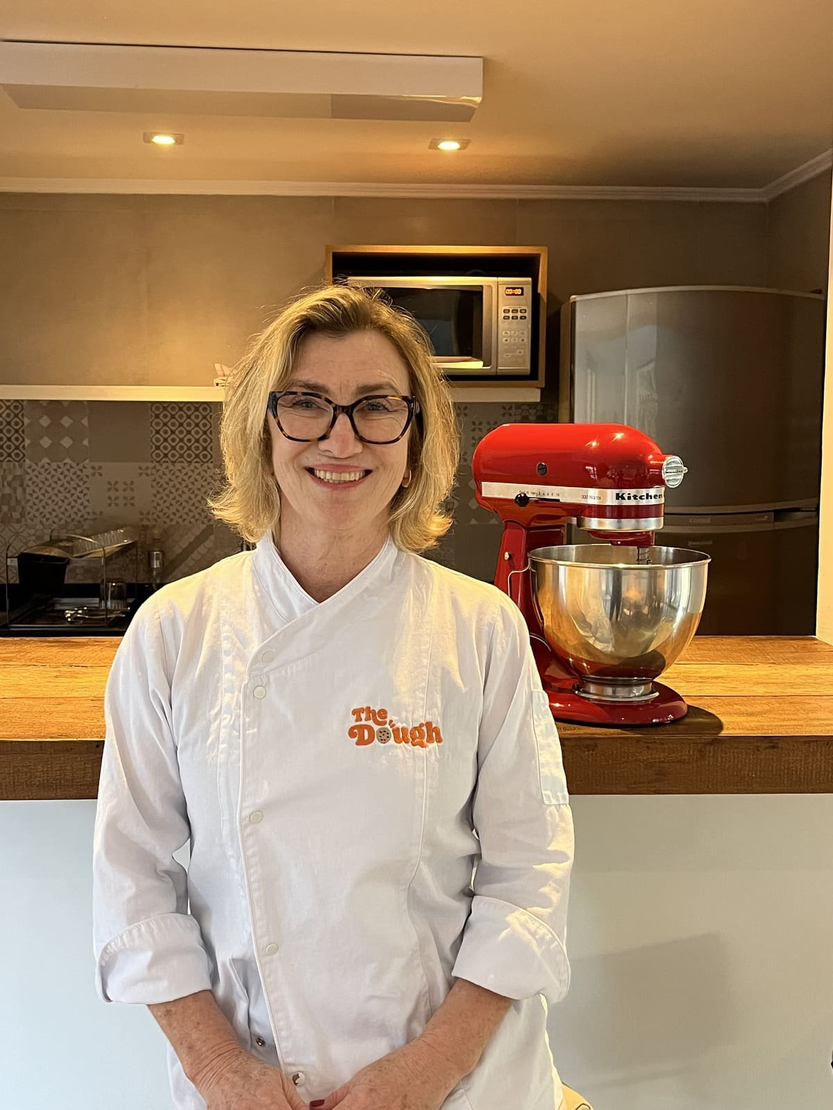 Chef Daniela na cozinha, ao lado da batedeira, com o jaleco The Dough